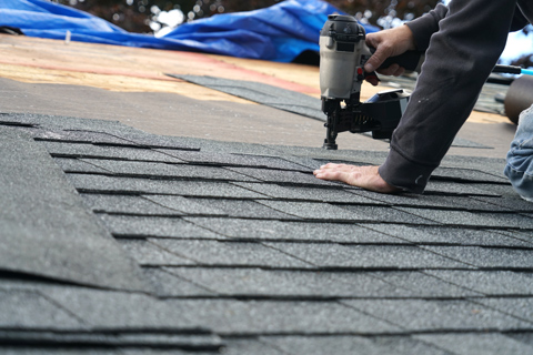 roofer using nail gun to install new shingle on roof repairs